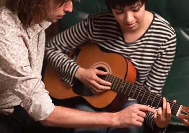 Young Musician Teaches Female Student To Play the Guitar